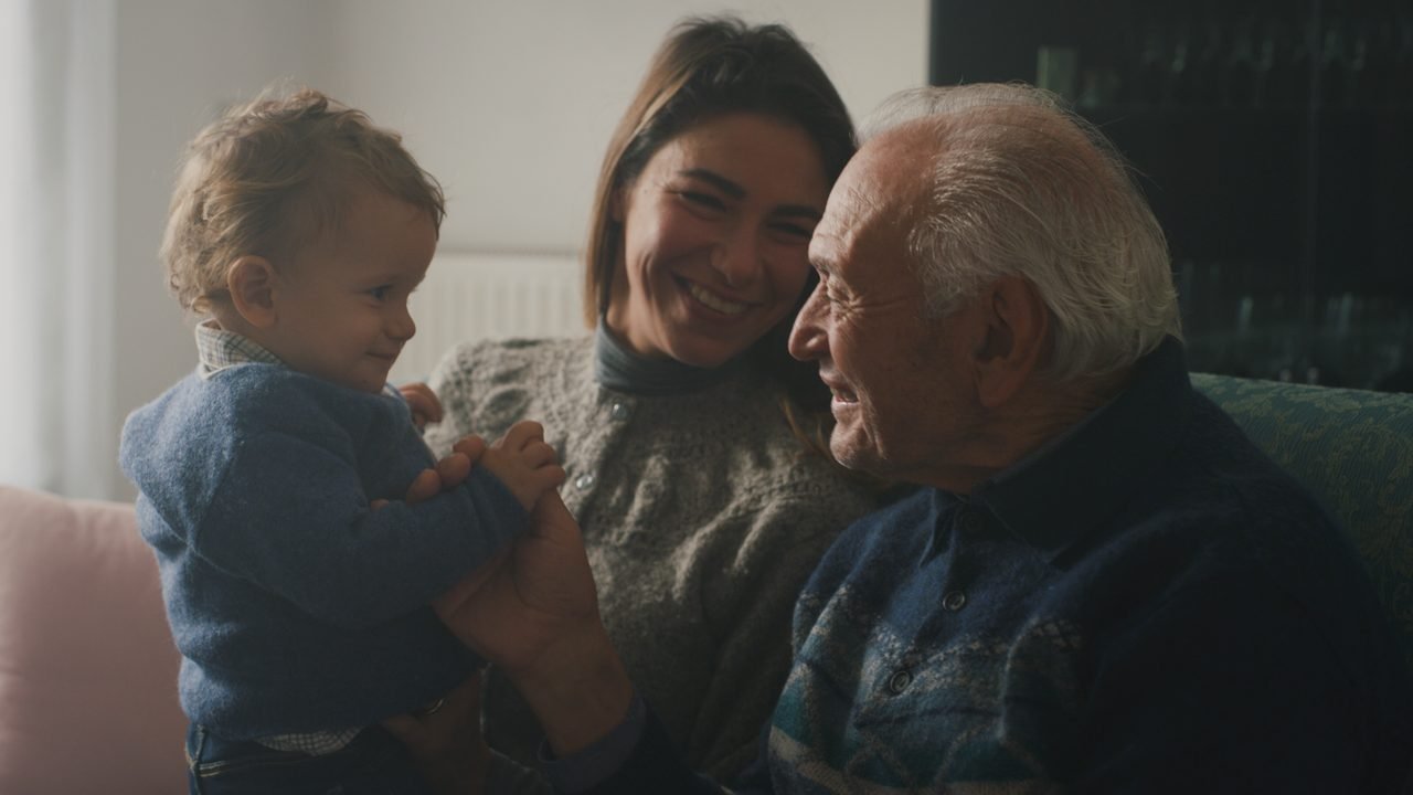 Un abuelo, su hija y el bebé de ella sentados juntos en un sofá en casa.